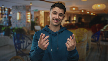 Young man in a hotel making a come here gesture, wearing a blue hoodie, set in an indoor setting...