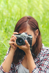 Vertical Asian Women with vintage film camera take a photo. Smiling female photographer look at photo from professional camera outdoor. Vertical photo of young woman shoot photo in green nature park