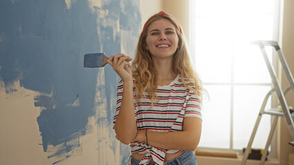 Woman painting wall in new home living room with blue color and smiling, showing happiness in home...