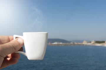 Man holds a cup of coffee in front of the sea