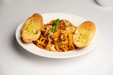 Spicy Penne Vegetarian Pasta — Penne tossed in a spicy tomato-based sauce with vegetables, served with two butter garlic toasts in a white plate on a white background.