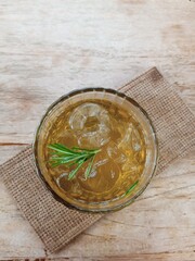 a glass of iced chamomile tea with rosemary leaf garnish on a wooden table