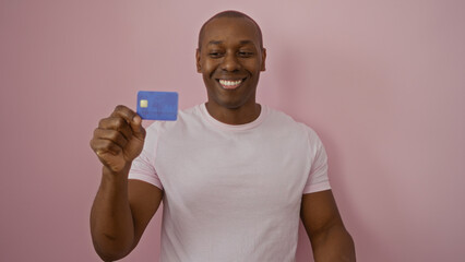 Man smiling holding credit against isolated pink wall, capturing financial confidence and charm.