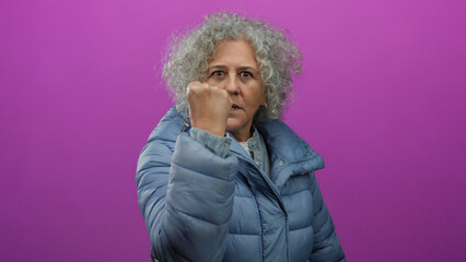 Woman with grey hair wearing blue jacket against pink background showing determination with...