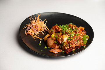 Hometown Chicken – A Pan-Asian style dish with tender chicken pieces tossed in spicy chilli sauce, served with fresh salad in a black plate on a white background.