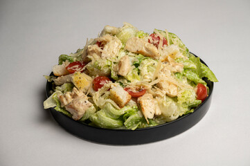 Caesar chicken salad served on a black plate with crisp lettuce, creamy parmesan garlic dressing, and crunchy croutons, placed on a white background.