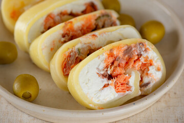 Farm cheese roll with salmon, olives and cream cheese on a plate, closeup.