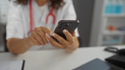 Woman using smartphone in clinic setting displaying focus on hands, technology, healthcare professional, medical workspace, indoor environment, communication tool, adult female.