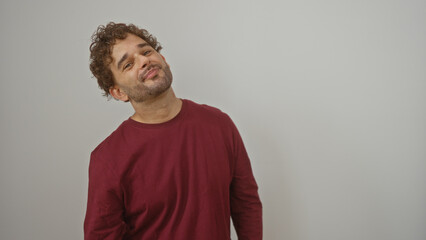 Young hispanic man smiling confidently against isolated white wall in casual red shirt showcasing style and charisma in modern portrait photography setting
