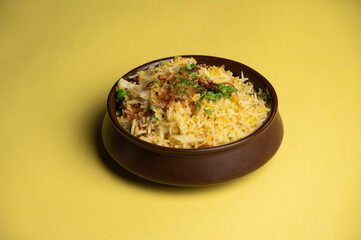 Basmati Pulao with green peas served in a traditional brown pot on a yellow background, highlighting its fragrant rice and vibrant color.