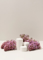 Beauty cosmetics product presentation scene made with white miniature columns surrounded by fresh lilac flowers on soft neutral background. Vertical photography.