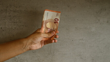 Closeup man holding euro banknotes against concrete background, displaying financial concept with physical currency.