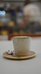 Table holds ceramic coffee cup with spoon on saucer in cozy restaurant setting indoors.