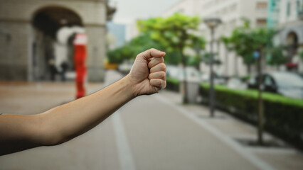 Man holding fist on street with blurred cityscape showing vibrant outdoor urban setting and clear...
