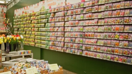 Blurred flower shop display featuring vibrant seed packets in soft focus, showing colorful tulips in the foreground and shelves lined with garden supplies in the background.