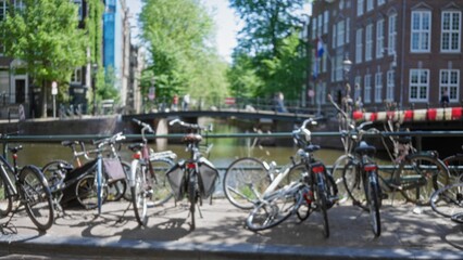 Bicycles parked near amsterdam canal with defocused bridge and lush greenery, capturing the essence of urban life and dutch culture in the netherlands.