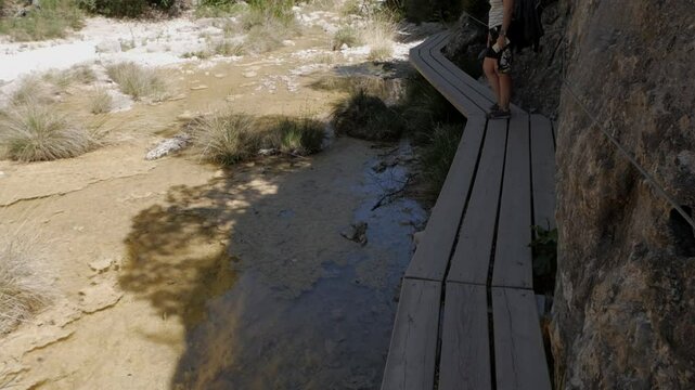 Hiker walking on wooden trail at Parrizal de Beceite in sunny Spain wilderness