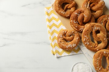 Tasty pretzels with salt on white marble table, flat lay. Space for text