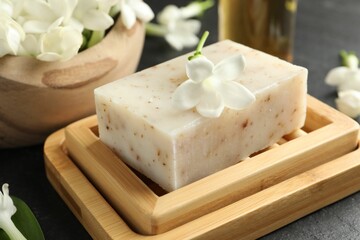 Bar of soap and jasmine flowers on black table, closeup