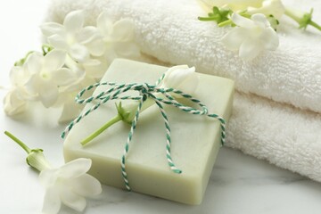 Bar of soap, jasmine flowers and towel on white marble table, closeup