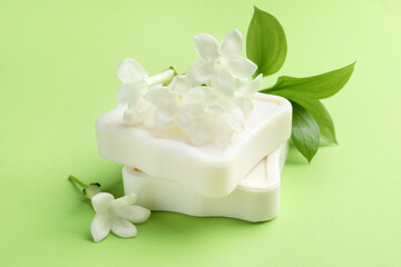 Bars of soap and jasmine flowers on light green background, closeup