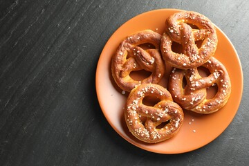 Tasty pretzels with salt on black table, top view. Space for text