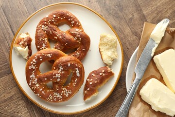 Tasty pretzels with salt and butter on wooden table, flat lay