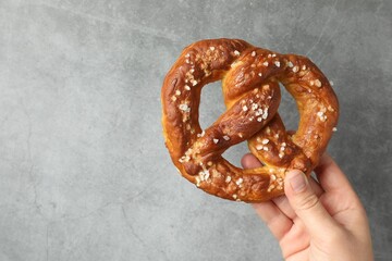 Woman with tasty pretzel near grey textured wall, closeup. Space for text