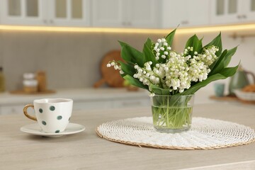 Bouquet of beautiful lily-of-the-valley and cup on wooden table in kitchen
