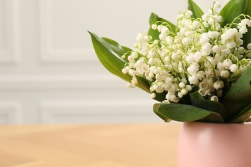 Beautiful lilies of the valley flowers in vase on wooden table, closeup. Space for text