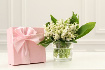 Beautiful lilies of the valley flowers and gift on white table