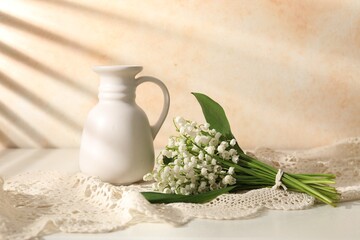 Beautiful lilies of the valley flowers and vase on white table near beige wall
