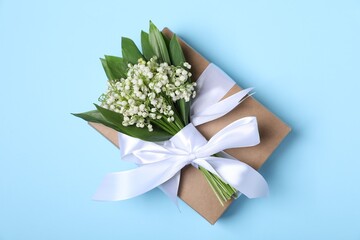 Beautiful lily-of-the-valley flowers and gift on light blue background, top view
