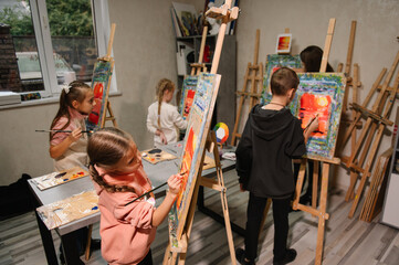Childs enjoy painting in workshop. Art lesson. Kids draw pictures in art class. Group of school children drawing with brush landscapes on easel. Education and learning concept. Mix and combine colors.