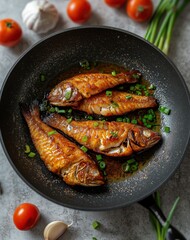 top view of golden fried fish in a black pan with oil and green onions next to it on a grey concrete table.
