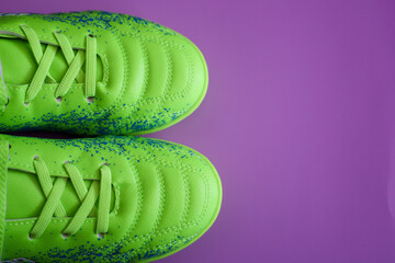 From above, a pair of bright green soccer cleats with blue speckles are visible on a purple...