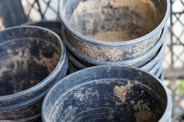 In the foreground, black plastic plant pots are stacked on top of each other, some with remnants of dry soil inside. Behind them is a blurred background with a plastic mesh.