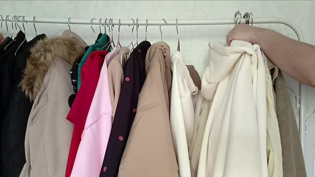 A woman's hand takes a lot of clothes on hangers from the clothes rack. A large rack with clothes hangers. Clothing store. The concept of clothing sales .stocks, clutter.