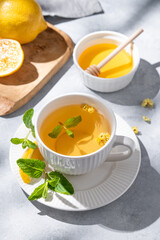 Cup of herbal tea with lemon, honey and mint on light background with citrus fruits