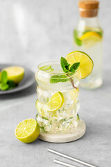 Mojito cocktail in a glass with lime, mint and ice on a textured background with natural light and bottle.