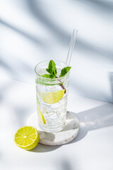 Mojito cocktail in a glass with lime, mint, ice and tube on a white blue background with shadows.
