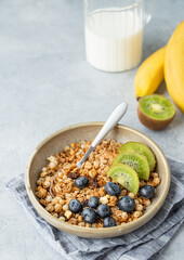  Homemade baked granola or muesli in a bowl with kiwi and blueberries on a light background