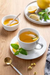 Cup of herbal tea with lemon, honey and mint on wooden tabletop with citrus fruits