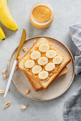 Peanut butter toast with banana on a plate on a light background with fruits and morning shadow.