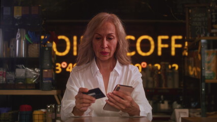 An old woman uses a credit card to shop on a smartphone. Senior female makes a purchase in an online store. Order online, enter the card number.