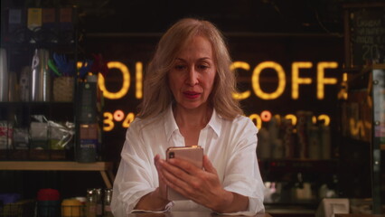 An old woman writes messages on a smartphone. The senior female communicates in a chat or messenger. Prints a letter on the touchscreen.