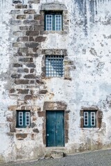 Weathered Stone Facade with Teal Door and Windows, Angra do Heroismo, Azores. Rustic close-up of an old stone building with a textured white and grey facade, featuring a teal wooden door