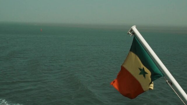Ralenti du drapeau du S&eacute;n&eacute;gal flottant au vent sur un bateau en mer &ndash; symbole national en mouvement avec l&rsquo;oc&eacute;an en arri&egrave;re-plan, tourn&eacute; depuis l&rsquo;embarcation en Casamance