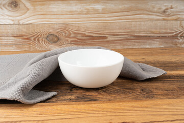 Empty white bowl on table, porcelain plate on wooden tabletop and grey tablecloth, minimal