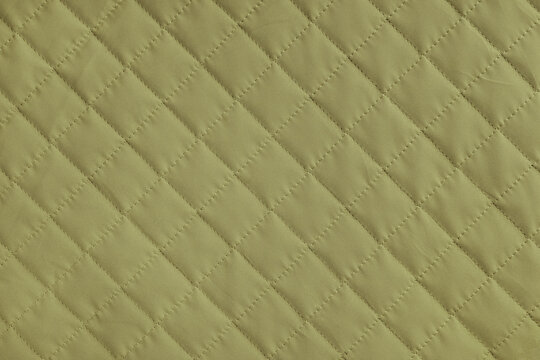 Checkered, diamond stitching pattern, khaki quilted fabric background. Blanket or puffer jacket, stitch rhombus texture close up, macro. Wallpaper, backdrop.